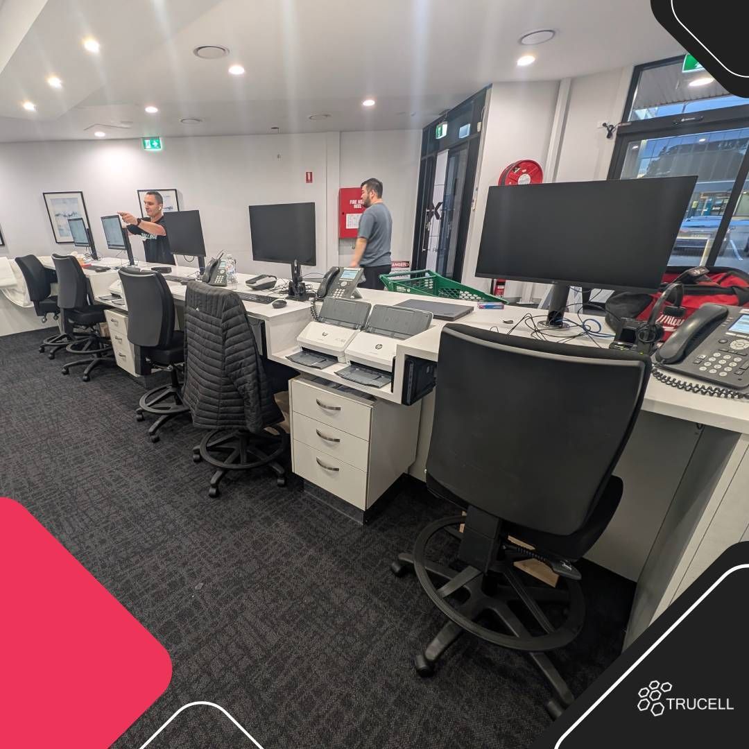 Completed Medical Imaging Erina front-desk fit-out: dual-monitor reception workstations, HP document scanners, 3CX VoIP handsets, drawer pedestals, and staff configuring the line during commissioning