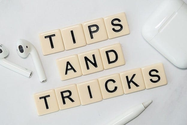 on a table with air pods and its container on the sides there are Scrabble tiles in the middle arranged and spelling tips and tricks.