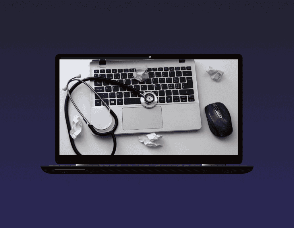 Opened laptop showing a laptop with a stethoscope above it, a mouse beside it and a few crumpled paper around