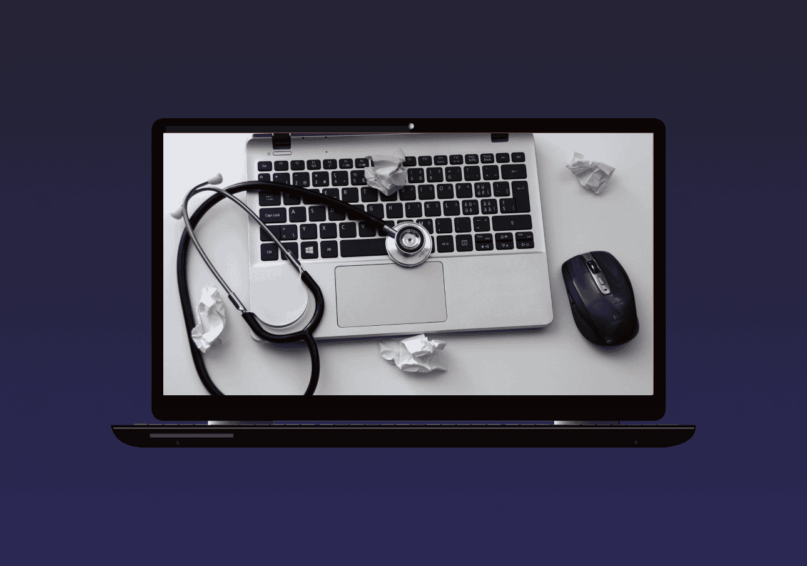 Opened laptop showing a laptop with a stethoscope above it, a mouse beside it and a few crumpled paper around