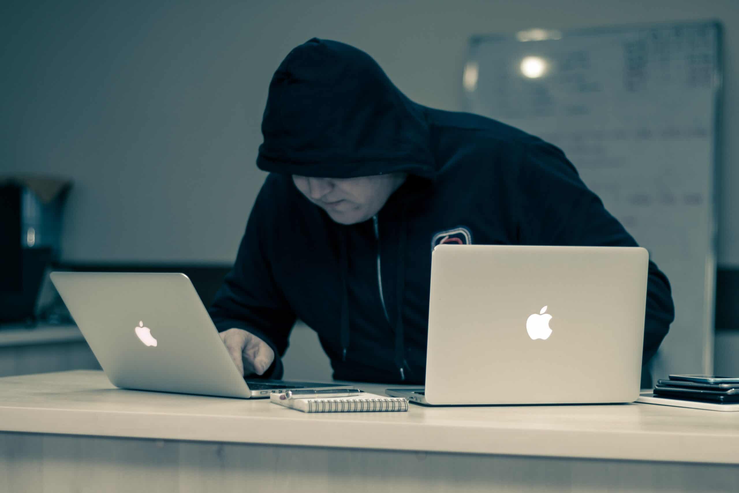 man handling two different apple laptop looking suspicious and a threat