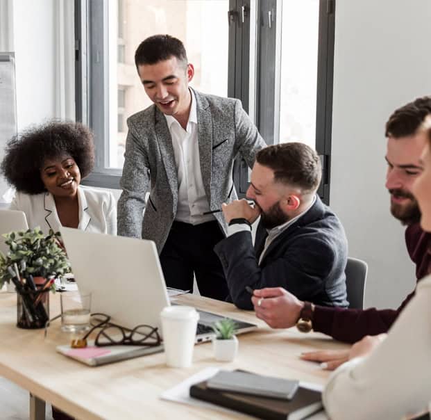 Group of people in a meeting while one guy is standing and pointing at a monitor