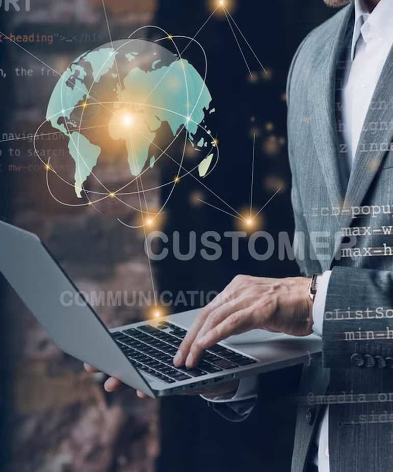 Man holding a laptop while pressing its keyboard with a hologram of globe with points made of light and are connected with lines