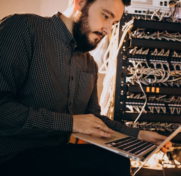 Guy using a laptop with a working server in his background