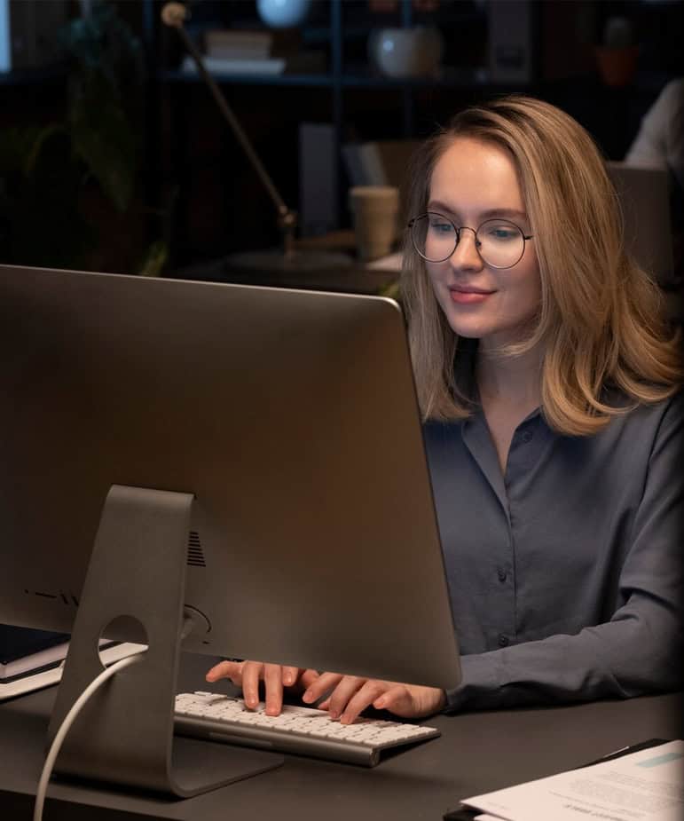 woman smiling facing a monitor and typing on a keyboard