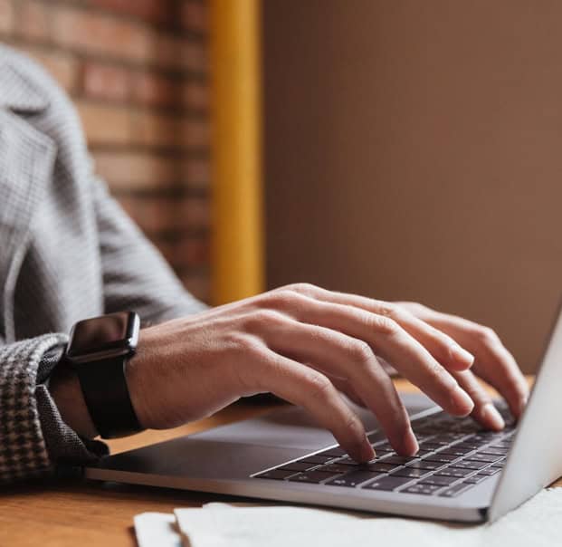 hand of a man wearing typing on a keyboard of an opened laptop