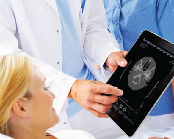 patient lying in bed with a doctor beside her showing an image of MRI scan using a tablet.